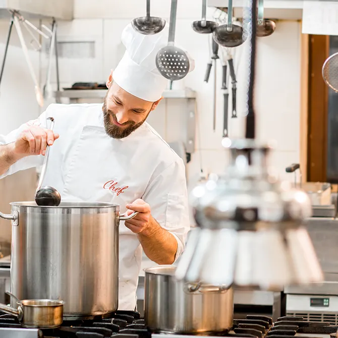 Een kok roert in een grote kookpot in een professionele keuken