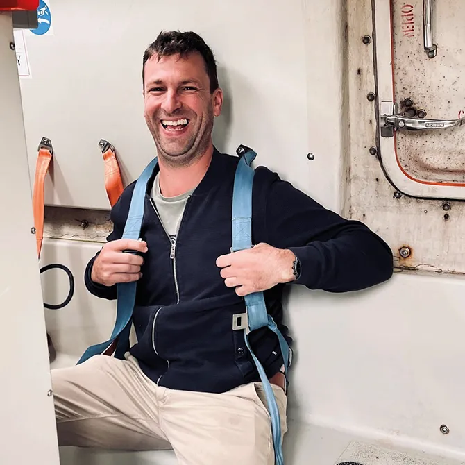 Een lachende cursist met een veiligheidsharnas aan boord van een schip