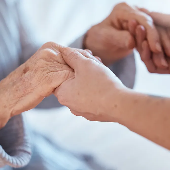 Een zorgverlener houdt de hand van een oudere persoon vast